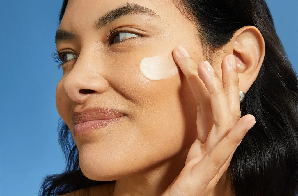 A young woman finishes the dewy look by swiping sunscreen on face