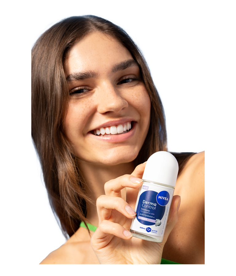 A young smiling woman turns her head while holding up NIVEA Derma Control Restore Deo Roll-On.