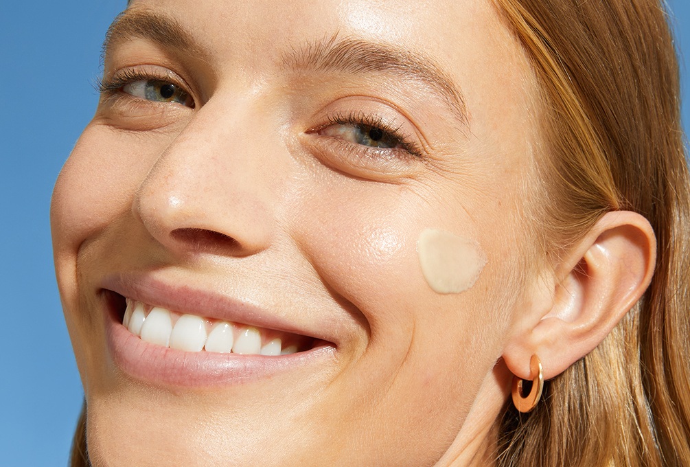A woman smiles with a swipe of daily fluid on her cheek.