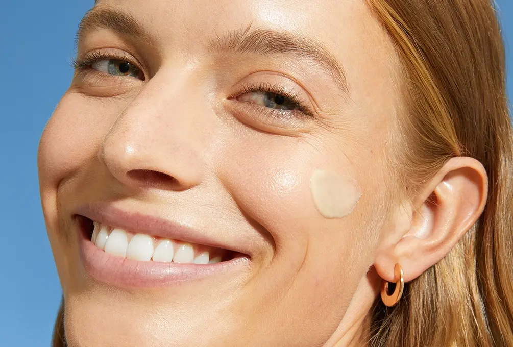 A woman smiles with a swipe of daily fluid on her cheek.
