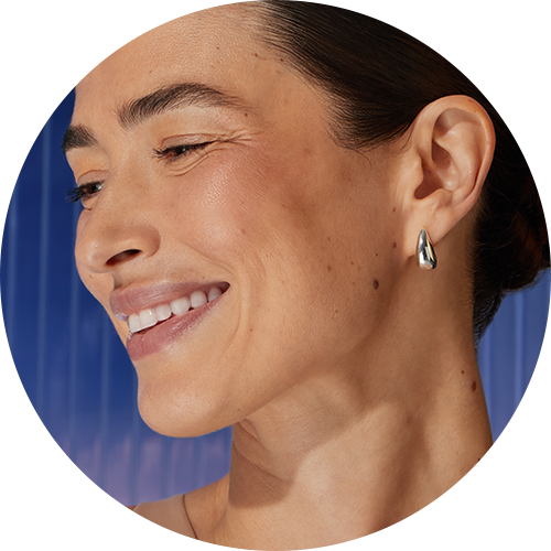 Nainen hymyilee, kallistaen päätään sivulle.