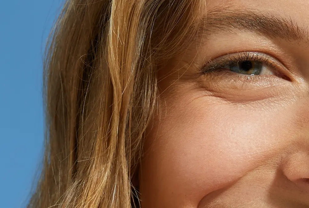A close-up of a smiling woman's eye and smooth cheek area.