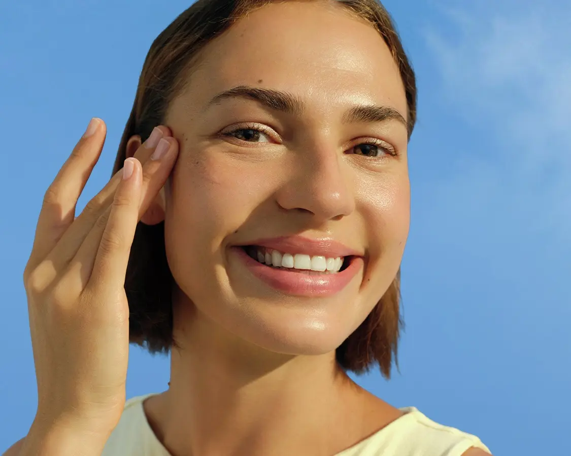 A young woman smiles and touches her temple.