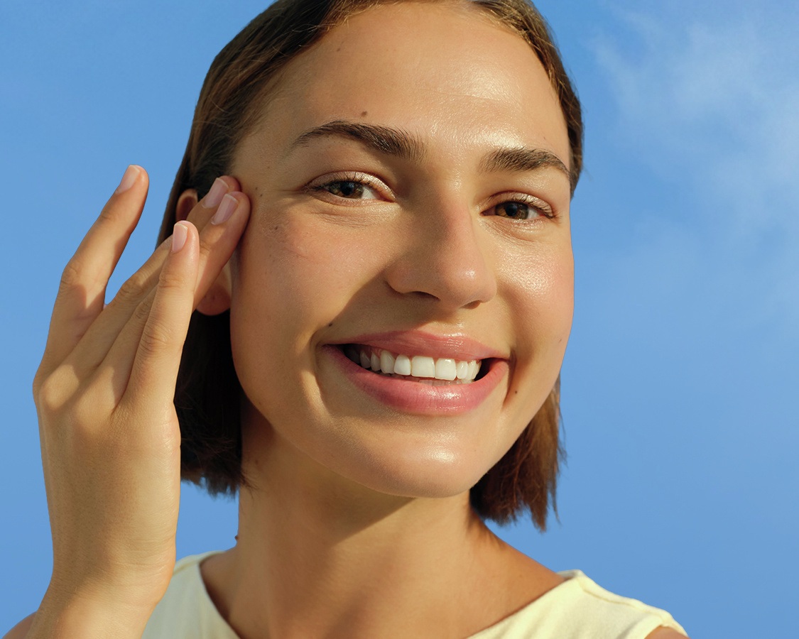 A young woman smiles and touches her temple.