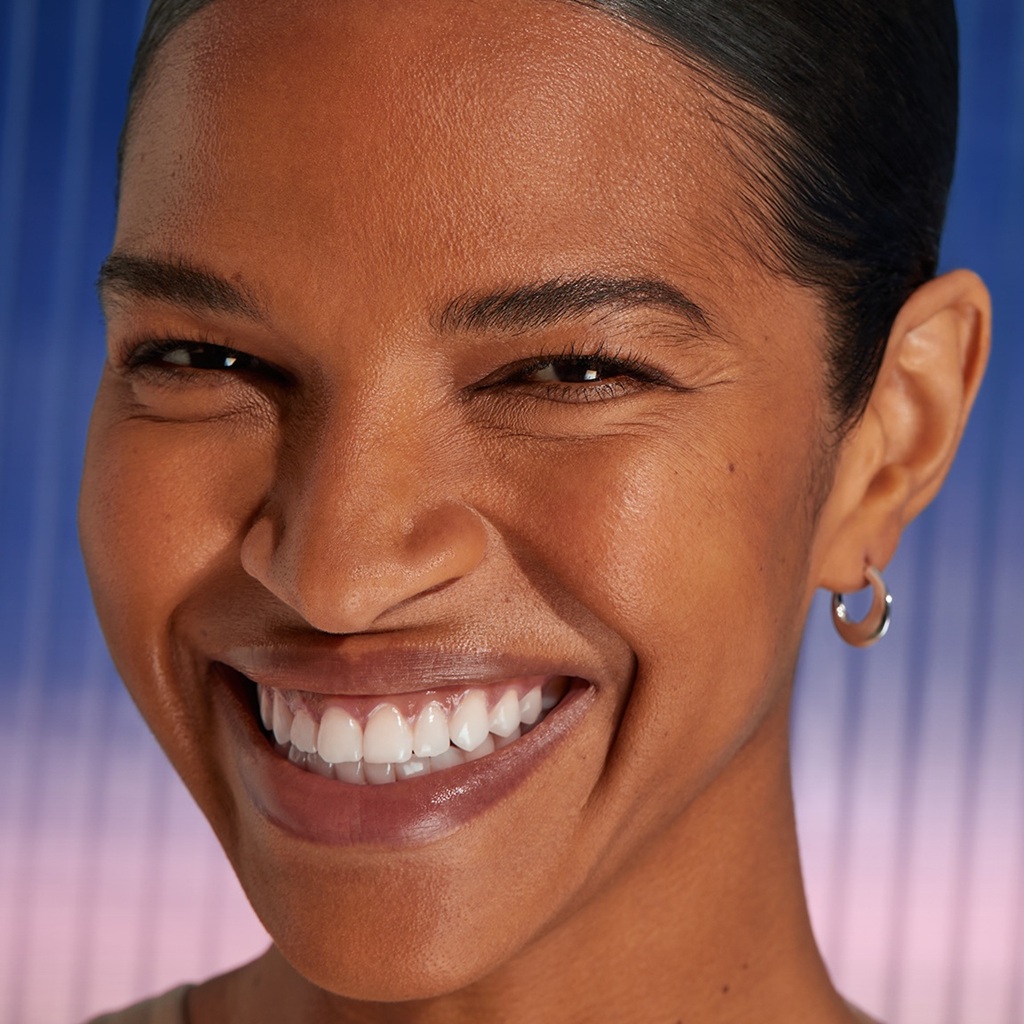 A woman smiles ahead, showing her smooth, youthful-looking complexion.