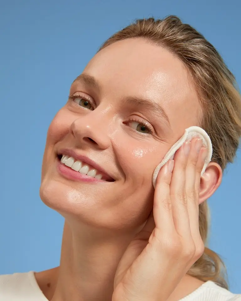 Blond ung kvinna som applicerar en flytande peeling med en bomullspad