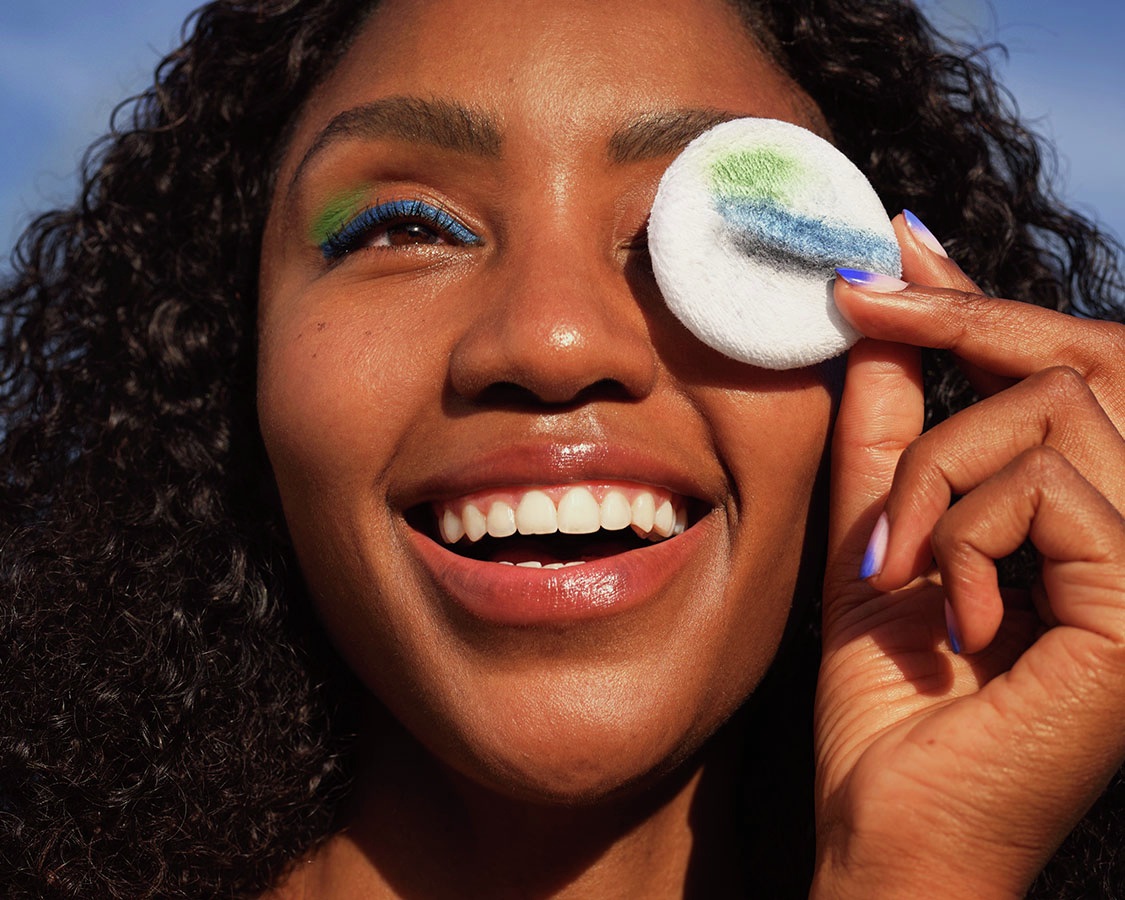Woman smiling with cotton pad over eye showing blue and black makeup residue