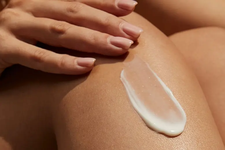 A woman's hand applies a swipe of vitamin body serum to her knee.