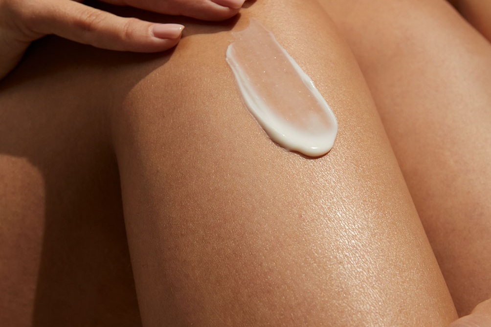 A woman's hand applies a swipe of vitamin body serum to her knee.