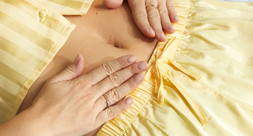 A woman's pair of hands places her hand on her tummy
