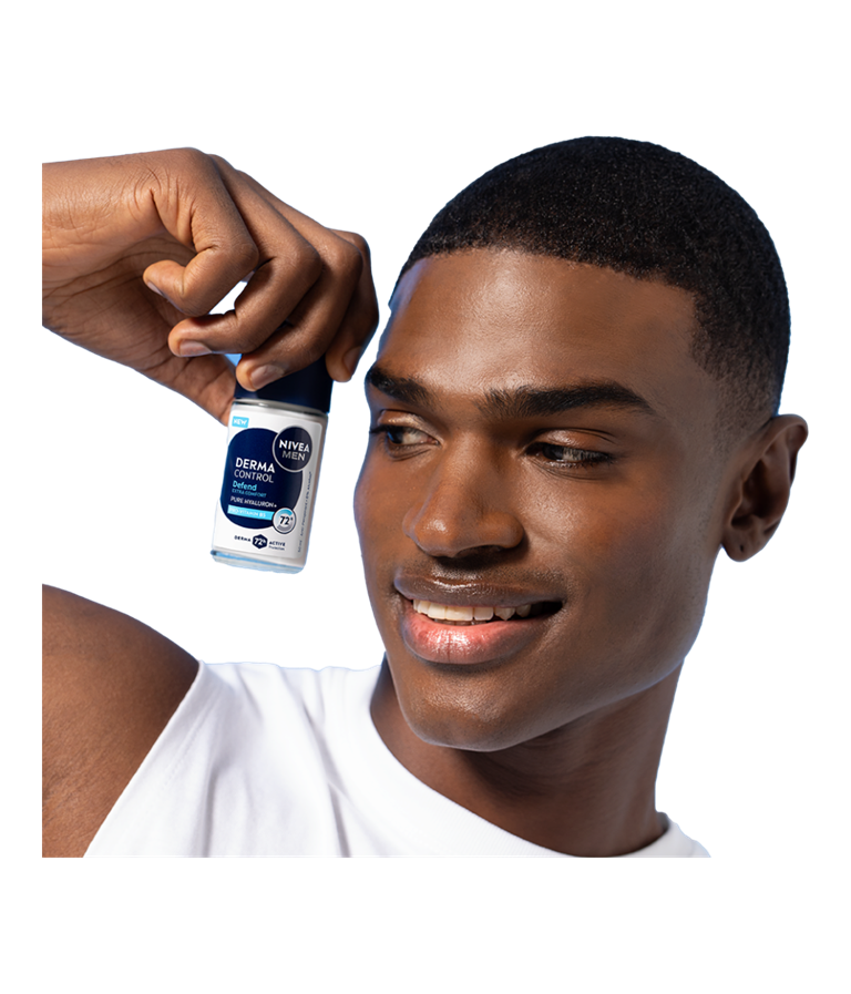 A young smiling man looks to the side while holding up NIVEA MEN Derma Control Defend Deo Roll-On.