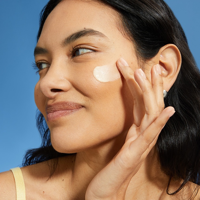 A young woman finishes the dewy look by swiping sunscreen on face