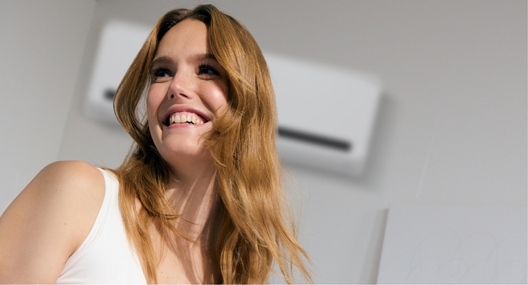 A woman with healthy skin smiling in front of an air conditioner
