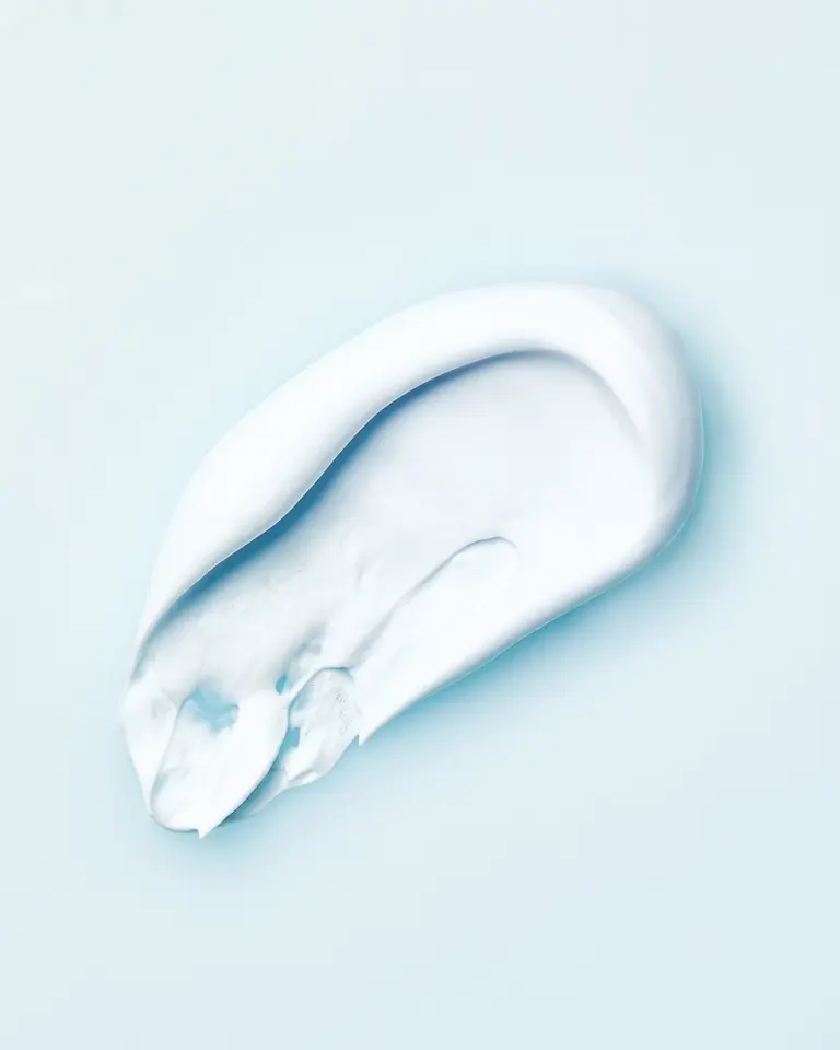 Thick swipe of white skincare cream with a smooth, glossy texture on a pale blue background