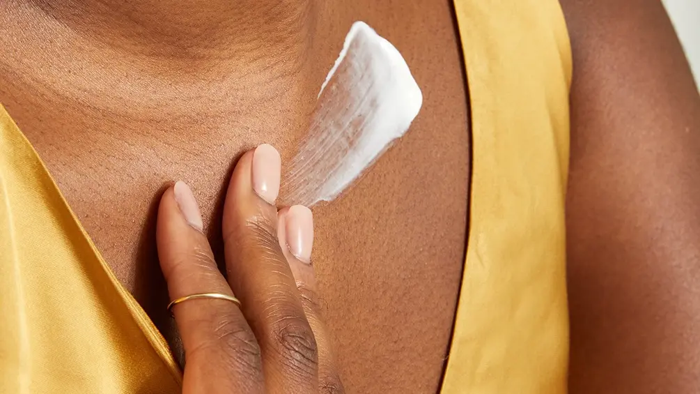 A close-up of a woman swiping Q10 body cream on her décolleté.