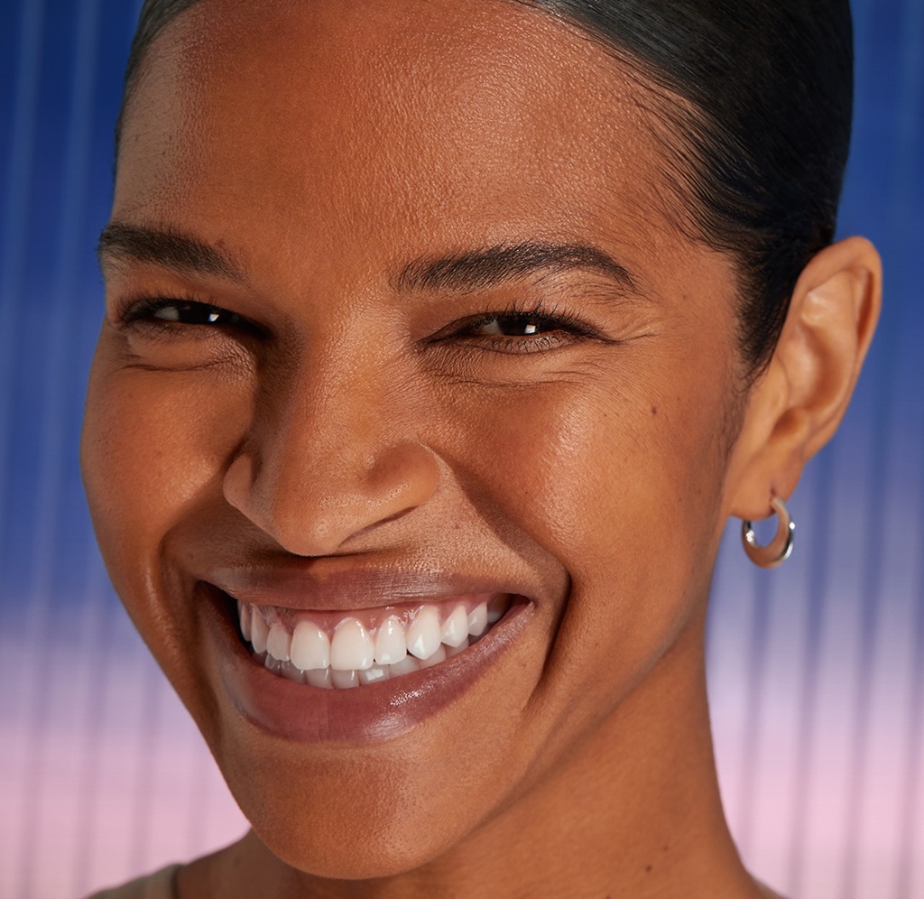 A woman smiles ahead, showing her smooth, youthful-looking complexion.