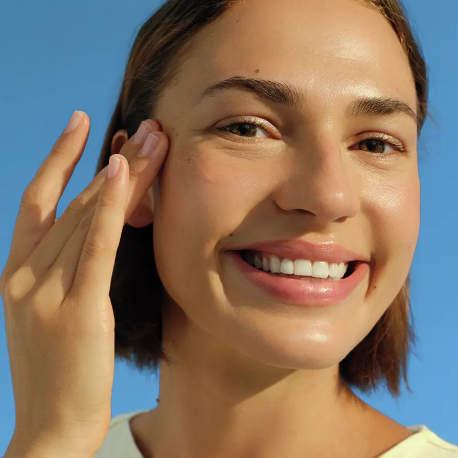 A young woman smiles and touches her temple.