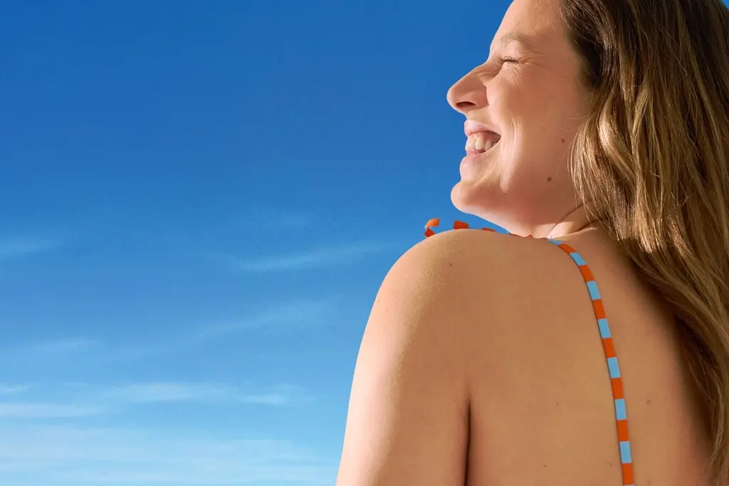 Smiling woman in a swimsuit enjoying the sunshine under a clear blue sky.