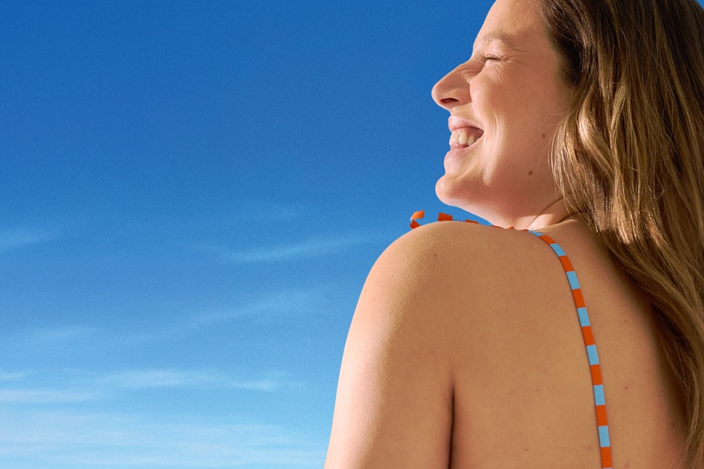 Smiling woman in a swimsuit enjoying the sunshine under a clear blue sky.