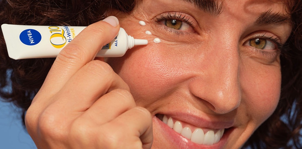 A woman smiles while applying NIVEA Q10 eye cream around her eye