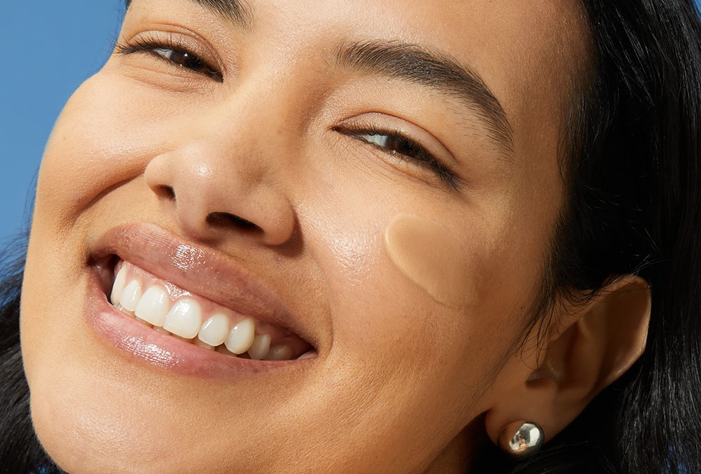 A woman smiles with a swipe of daily fluid on her cheek.