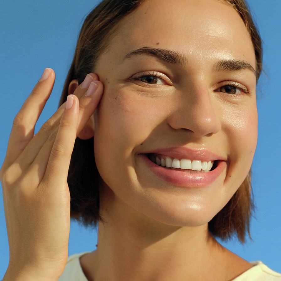 A young woman smiles and touches her temple.