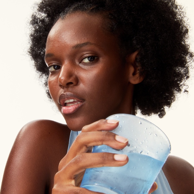 a young woman holding a glass of water looking into the camera