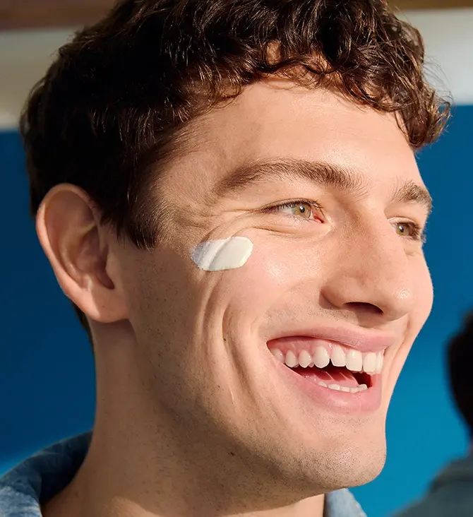 A man looks to the side, smiling with a swipe of NIVEA MEN Sensitive Daily Protect Moisturiser on his cheek.