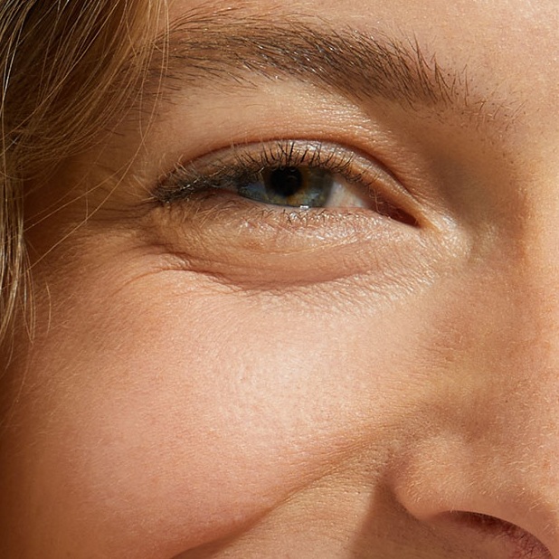 A close-up of a smiling woman's eye and smooth cheek area.