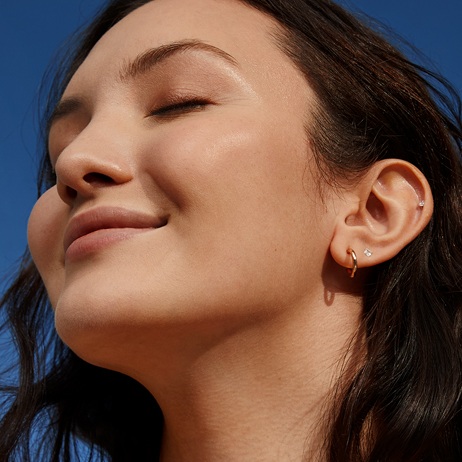 A young woman smiles with eyes closed, showing the glowing skin of her face and neck.