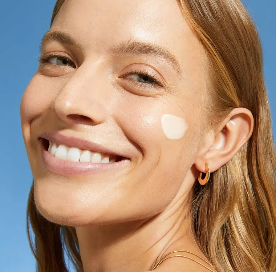 A woman smile with NIVEA SUN 2in1 Primer Daily UV Serum on her cheek.