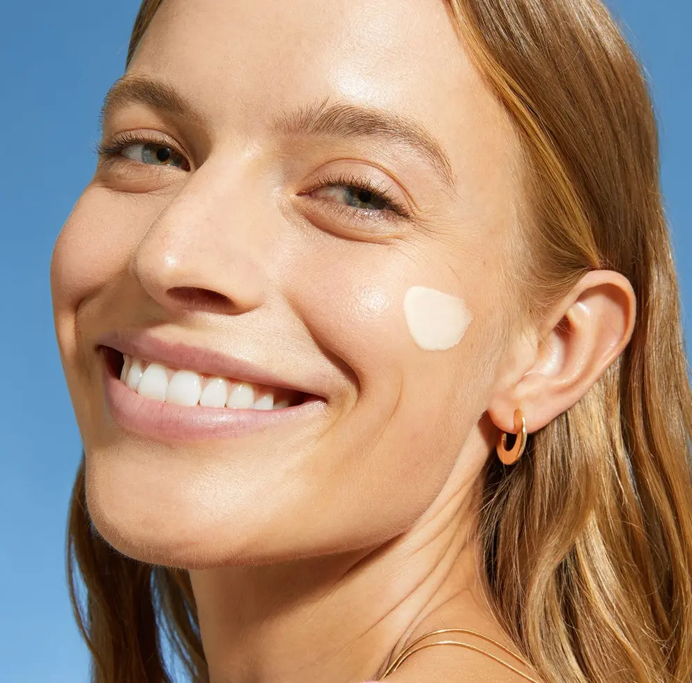 A woman smile with NIVEA SUN 2in1 Primer Daily UV Serum on her cheek.
