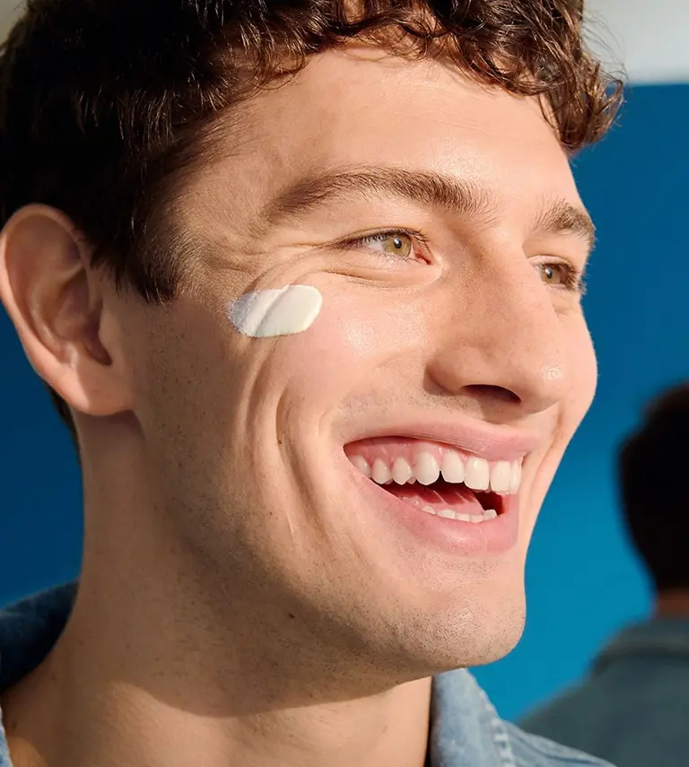 A man looks to the side, smiling with a swipe of NIVEA MEN Sensitive Daily Protect Moisturiser on his cheek.