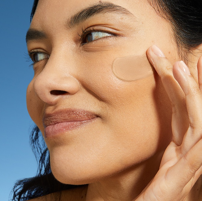 A woman smiles while swiping on daily fluid to her cheek.