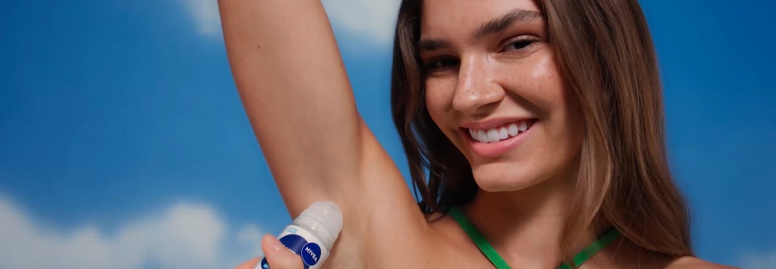 A young smiling woman has a lifted arm and applies NIVEA Derma Control Defend Deo Roll-On to her underarm.