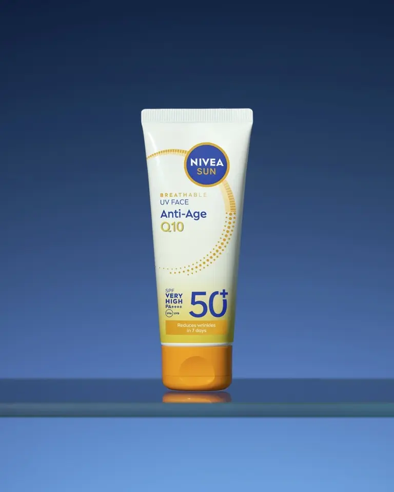 White tube of NIVEA Sun Breathable UV Face Anti-Age Q10 sunscreen SPF 50+ with orange cap on blue background