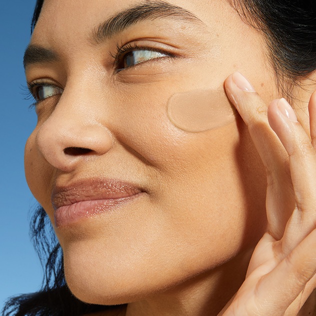 A woman smiles while swiping on daily fluid to her cheek.