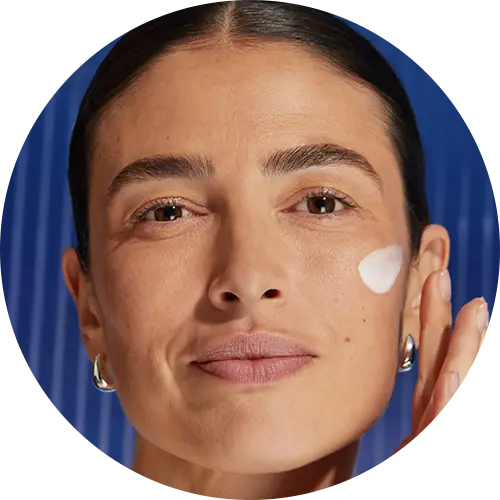 A woman gazes while swipign serum product on her cheek.